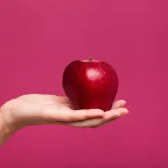 Dłoń trzyma lśniące, czerwone jabłko. Czy od jabłek się tyje? To pytanie nurtuje wiele osób dbających o linię.