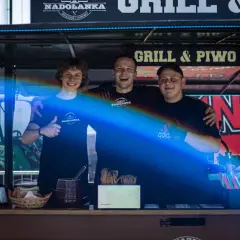 Trzech uśmiechniętych mężczyzn za ladą cateringową z napisem "Grill & Piwo".