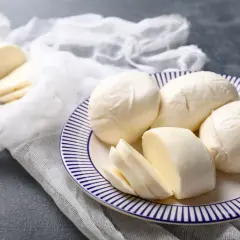 Świeża mozzarella na talerzu, pokrojona i w całości. Czy mozzarella podnosi cukier? Ten ser jest niskowęglowodanowy.