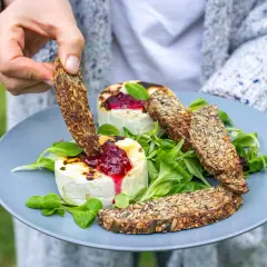 Ręka zanurza chrupki chleb pełen ziaren w grillowanym serze z konfiturą. Czy chleb tuczy? Ten z pewnością jest zdrowy!
