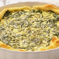 Pyszny quiche ze szpinakiem w białej formie, idealny pomysł na to, jak jeść szpinak. Złociste ciasto i kremowe nadzienie.