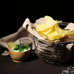 Koszyk pełen chipsów tortilla, obok miseczka z dipem i ziołami. Czy chipsy tortilla są zdrowe? To zależy od składników i sposobu przygotowania.