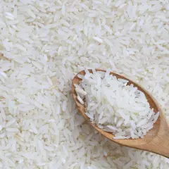 Łyżka białego ryżu na tle rozsypanych ziaren. Czy ryż ma gluten? Nie, ryż jest naturalnie bezglutenowy.