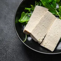 Trzy kawałki tofu na talerzu z zielonymi liśćmi i żółtym kwiatkiem. Czy tofu to nabiał? To pytanie często zadawane przez osoby na diecie roślinnej.