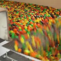 Kolorowe drażetki spadają z taśmociągu. Czy skittles są bezglutenowe? To pytanie nurtuje wielu łasuchów.