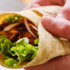 Ręce trzymają świeżą tortillę z sałatą, cebulą i mięsem. Zastanawiasz się, ile kalorii ma tortilla?
