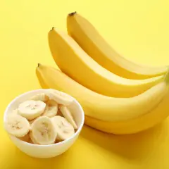 Kilka dojrzałych bananów i miseczka pokrojonych bananów na żółtym tle. Banany a refluks – czy są bezpieczne?
