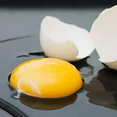 Rozbite jajko na ciemnym tle. Żółtko lśni, a skorupka czeka na usmażenie. Zastanawiasz się nad jajko smażone kcal?
