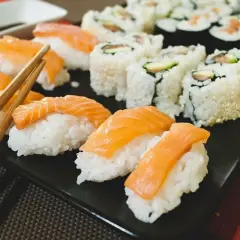 Pyszne sushi na diecie: nigiri z łososiem i rolki z awokado na czarnej tacy, gotowe do spożycia.