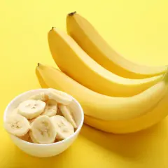 Pytanie: czy banany są kaloryczne? Na żółtym tle pęczek żółtych bananów i miseczka z plasterkami banana.