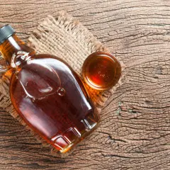 Butelka syropu klonowego i mała miseczka z tym samym płynem. Syrop glukozowy to słodki dodatek.