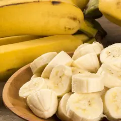 Cały banan i pokrojone kawałki na drewnianej desce. Dowiedz się, ile błonnika ma banan, by wzbogacić swoją dietę.