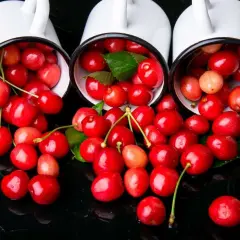 Czy czereśnie odchudzają? Sprawdźmy! Na zdjęciu soczyste, czerwone czereśnie wysypujące się z trzech białych kubków na czarnym tle.