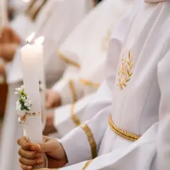 Dziecko trzyma ozdobioną świecę podczas komunii. Zastanawiasz się, ile kosztuje komunia na 30 osób?