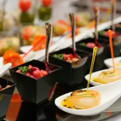 Eleganckie przekąski na imprezę: małe porcje w czarnych naczyniach i na łyżeczkach.