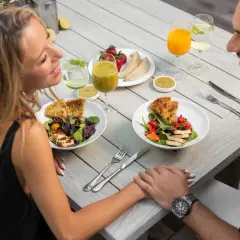 Romantyczny catering dla par. Uśmiechnięta para trzyma się za ręce przy stole z pysznymi sałatkami, owocami i napojami.