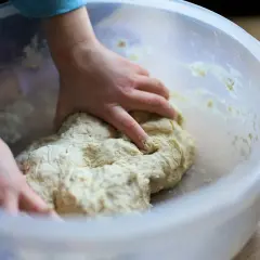Dziecko zagniata ciasto w misce. Czy weganie jedzą drożdże? Tak, drożdże to grzyby, więc są wegańskie.