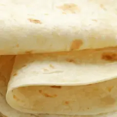 Stos cienkich, jasnych placków tortilli na drewnianym blacie. Czy tortilla jest zdrowsza od chleba? Zależy od składników!