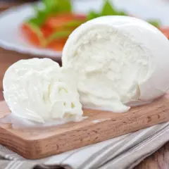 Świeża kulka mozzarelli na desce, w tle sałatka. Zastanawiasz się, ile kcal ma kulka mozzarelli?