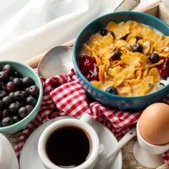 Śniadanie na tacy: płatki z jagodami, jajko na miękko, kawa i muffinka.