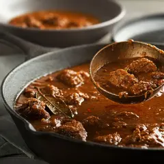 Gęsty, aromatyczny gulasz wołowy w żeliwnej patelni. Łyżka nabiera porcję mięsa. Dowiedz się, jak zagęścić gulasz bez mąki.