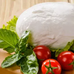 Kulista mozzarella, pomidorki i bazylia na desce. Czy mozzarella ma dużo białka? Tak, to świetne źródło białka!
