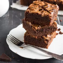 Pyszne ciasto dla odchudzających się: trzy czekoladowe brownie ułożone na talerzyku, obok widelec i kawałki gorzkiej czekolady.