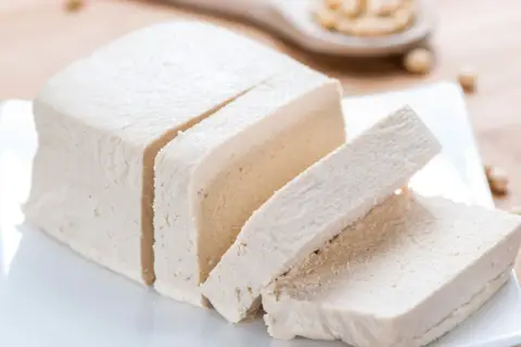 Kostka tofu, pokrojona w plastry, na białym talerzyku. Czy tofu to soja? Tak, to produkt z soi.