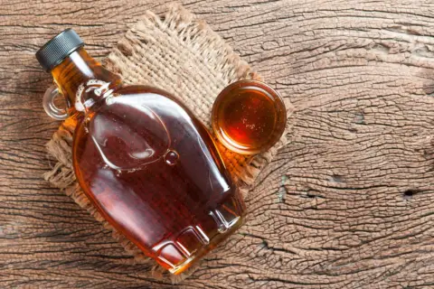 Butelka syropu klonowego i mała miseczka z tym samym płynem. Syrop glukozowy to słodki dodatek.