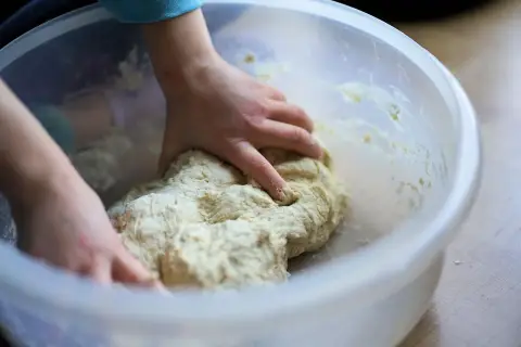 Dziecko zagniata ciasto w misce. Czy weganie jedzą drożdże? Tak, drożdże to grzyby, więc są wegańskie.