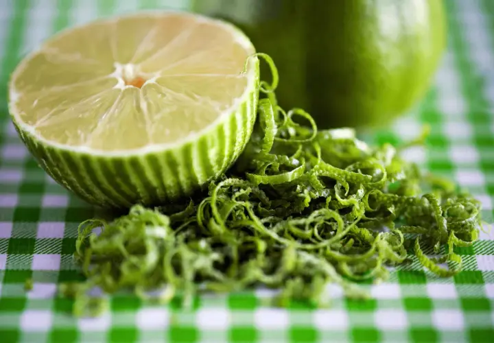 Połówka limonki i jej skórka na zielono-białej kratce. Czy limonka jest zdrowa? Tak, to cytrus pełen witamin!