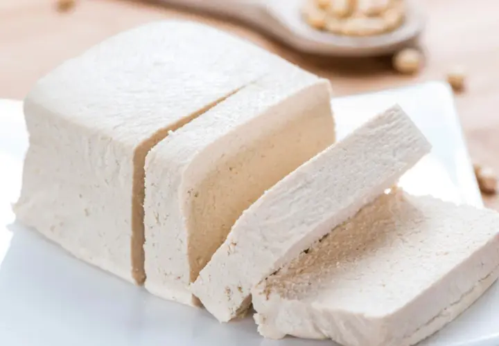 Kostka tofu, pokrojona w plastry, na białym talerzyku. Czy tofu to soja? Tak, to produkt z soi.