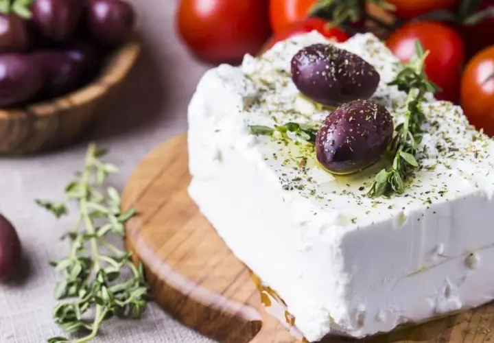 Kostka sera feta, polana oliwą i posypana ziołami, z oliwkami i pomidorkami w tle. Właściwości sera feta doceniane są w kuchni śródziemnomorskiej.