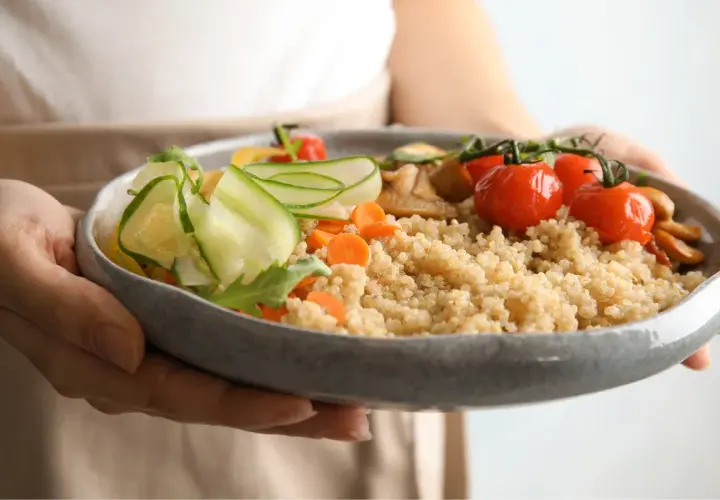 Miseczka pełna kaszy jaglanej z warzywami: pomidorkami, ogórkiem i marchewką. Świetna alternatywa, czym zastąpić ziemniaki.
