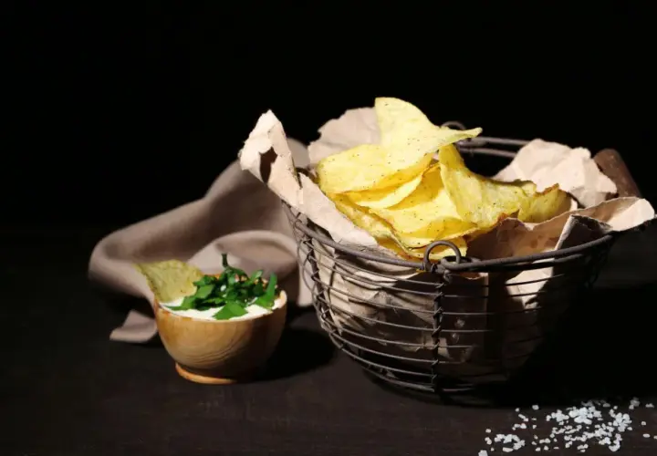 Koszyk pełen chipsów tortilla, obok miseczka z dipem i ziołami. Czy chipsy tortilla są zdrowe? To zależy od składników i sposobu przygotowania.