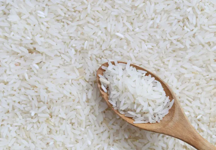 Łyżka białego ryżu na tle rozsypanych ziaren. Czy ryż ma gluten? Nie, ryż jest naturalnie bezglutenowy.