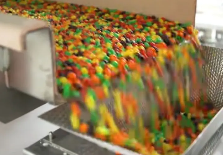 Kolorowe drażetki spadają z taśmociągu. Czy skittles są bezglutenowe? To pytanie nurtuje wielu łasuchów.