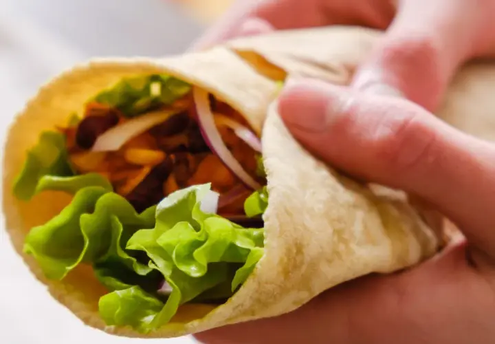 Ręce trzymają świeżą tortillę z sałatą, cebulą i mięsem. Zastanawiasz się, ile kalorii ma tortilla?