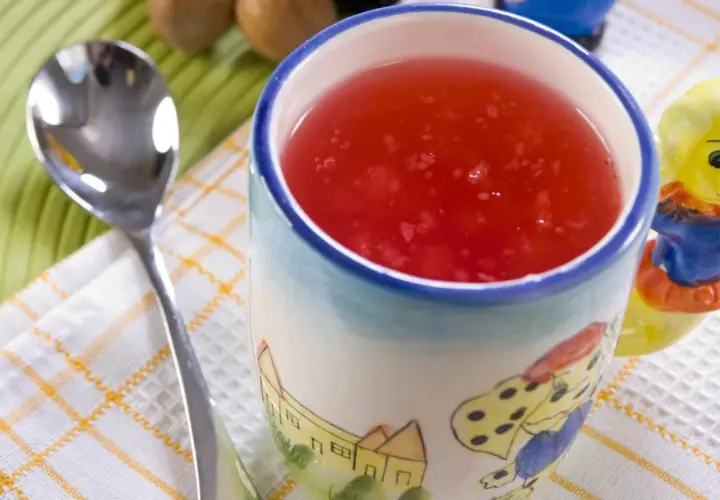 Czerwony kisiel w kubeczku z bajkowym wzorem, obok łyżeczka. Kisiel jest dobry na trawienie i lekkostrawny.
