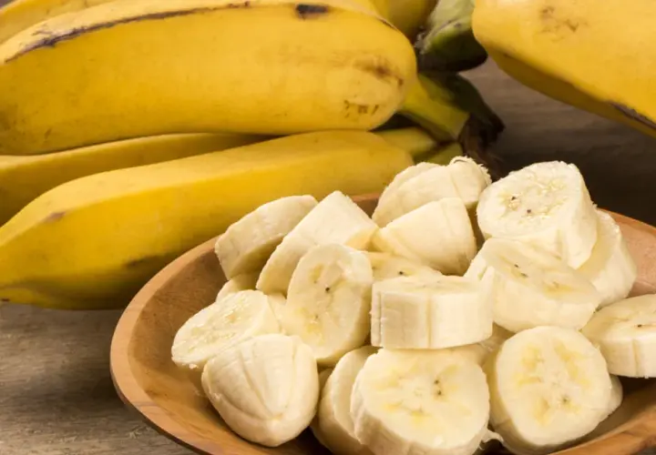 Cały banan i pokrojone kawałki na drewnianej desce. Dowiedz się, ile błonnika ma banan, by wzbogacić swoją dietę.