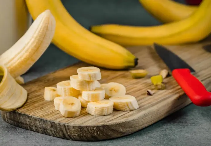 Plasterki banana na desce, idealne na pusty żołądek. Obok leży nóż z czerwoną rączką.