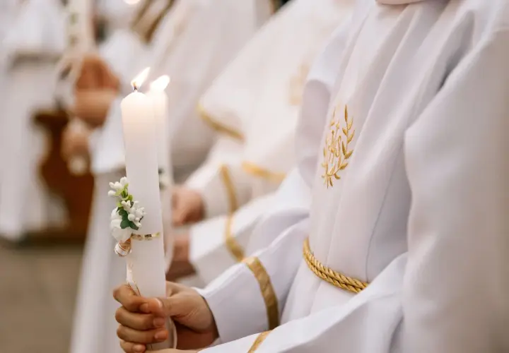 Dziecko trzyma ozdobioną świecę podczas komunii. Zastanawiasz się, ile kosztuje komunia na 30 osób?