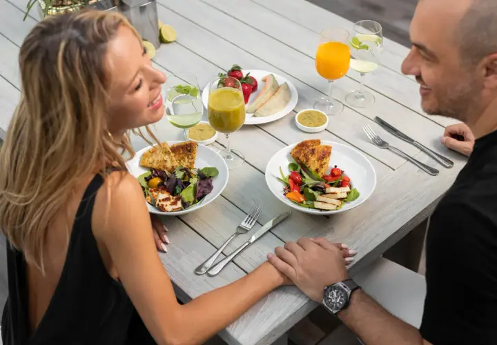 Romantyczny catering dla par. Uśmiechnięta para trzyma się za ręce przy stole z pysznymi sałatkami, owocami i napojami.