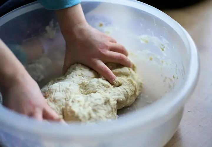 Dziecko zagniata ciasto w misce. Czy weganie jedzą drożdże? Tak, drożdże to grzyby, więc są wegańskie.