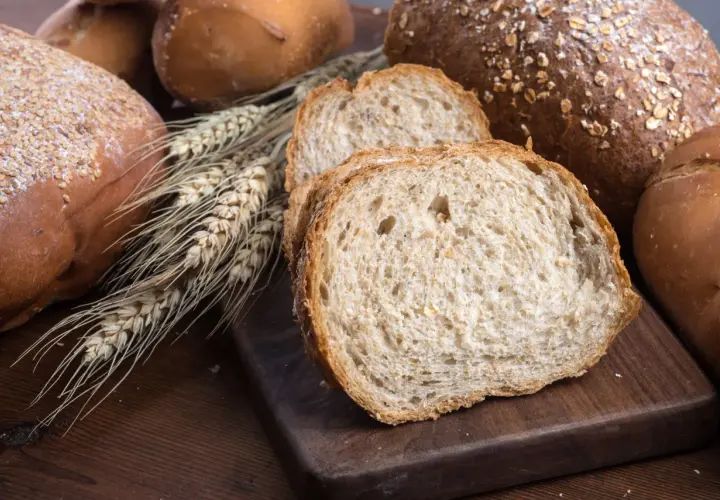 Różnorodne pieczywo, w tym bochenki z ziarnami i kromki chleba pełnoziarnistego. Idealne, gdy zastanawiasz się, jakie pieczywo przy odchudzaniu wybrać.