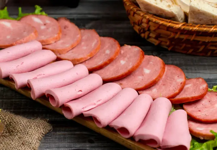 Na desce ułożone są różowe parówki i plastry wędliny. Zastanawiasz się, jakie wędliny są najzdrowsze?