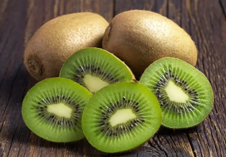 Kiwi na refluks. Dwa całe owoce kiwi i cztery przekrojone na pół, ukazujące zielony miąższ z czarnymi pestkami, leżą na drewnianym blacie.