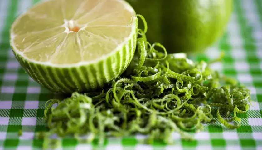 Połówka limonki i jej skórka na zielono-białej kratce. Czy limonka jest zdrowa? Tak, to cytrus pełen witamin!