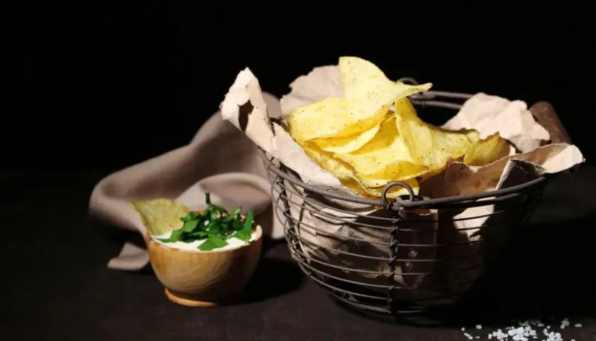 Koszyk pełen chipsów tortilla, obok miseczka z dipem i ziołami. Czy chipsy tortilla są zdrowe? To zależy od składników i sposobu przygotowania.