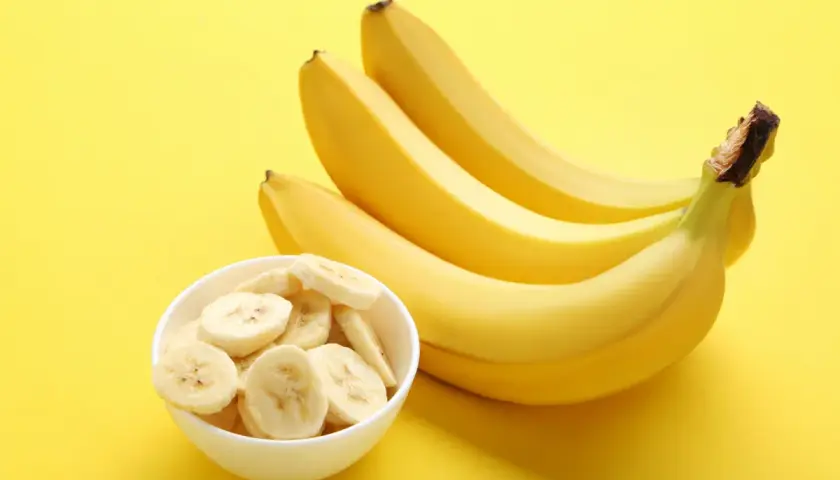 Kilka dojrzałych bananów i miseczka pokrojonych bananów na żółtym tle. Banany a refluks – czy są bezpieczne?